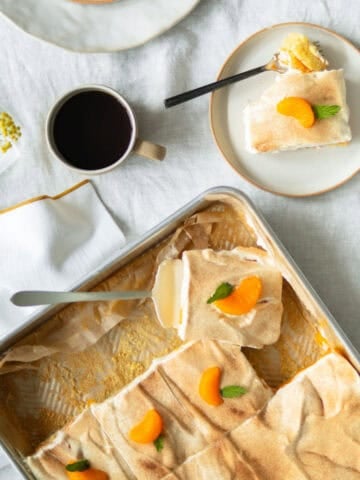 Orange cake with mandarin oranges in a cake pan with a cup of coffee.
