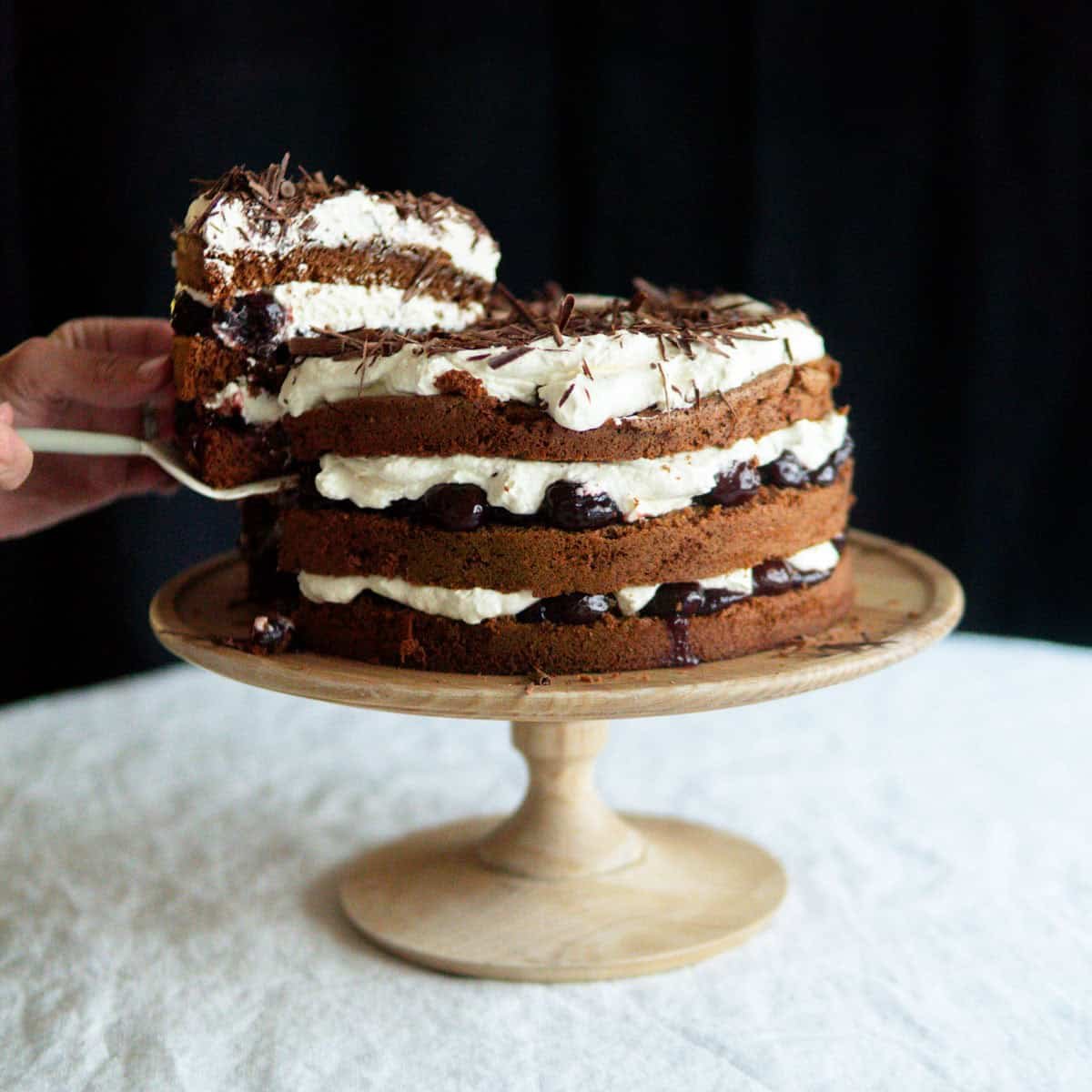 decorated Black Forest cake sitting on a wooden cake stand.