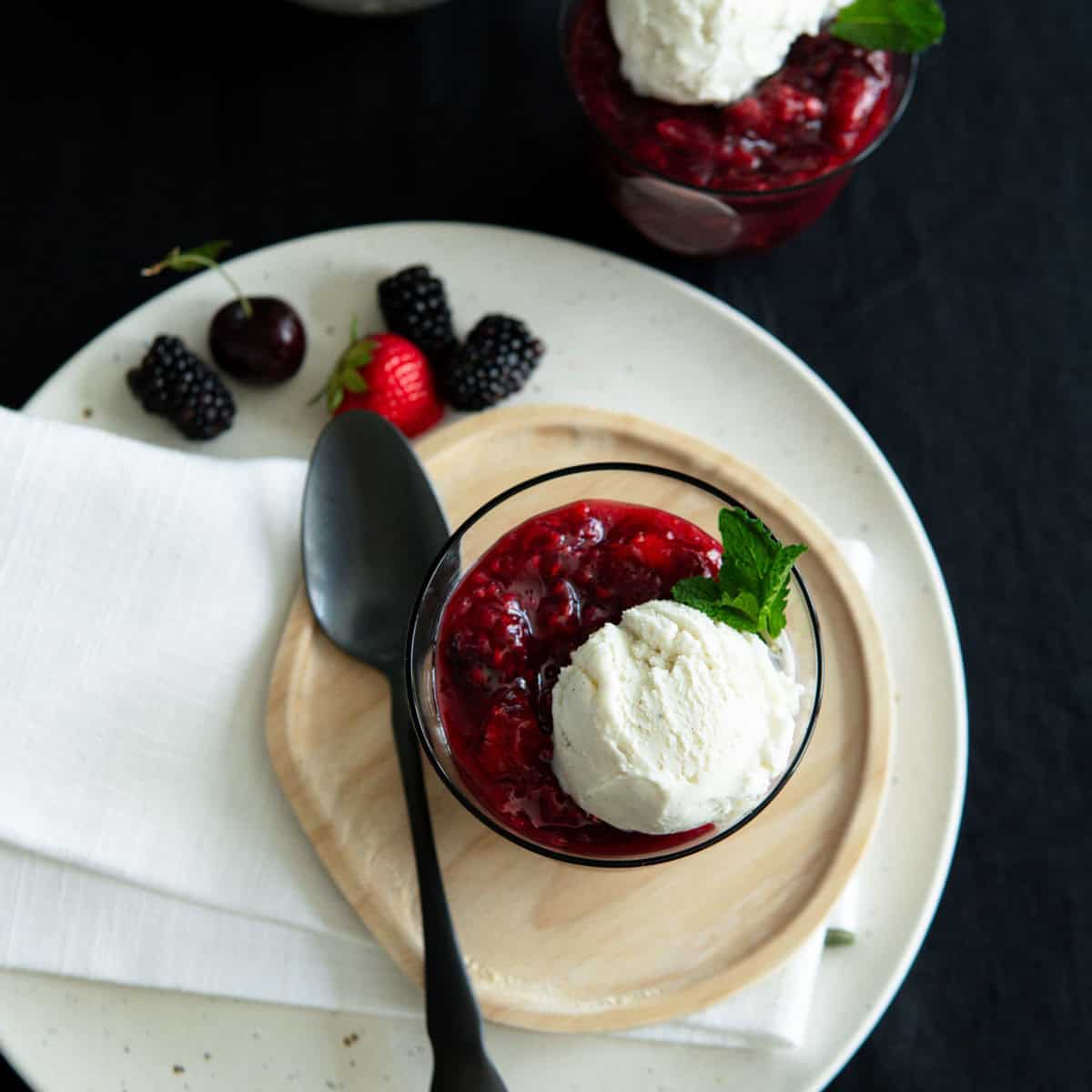 Berry sauce with vanilla ice cream in a glass cup with a spoon.