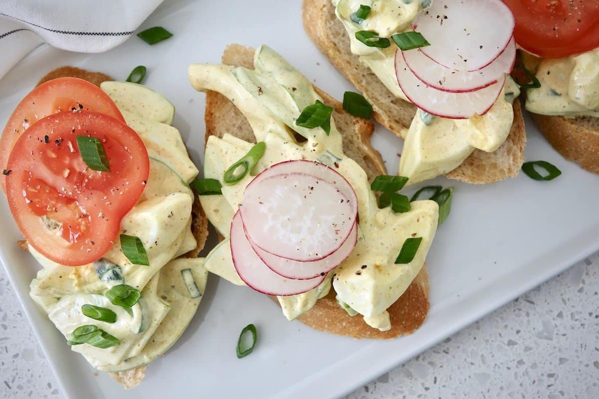 German curry egg salad served on baguette rounds with sliced radishes and sliced tomatoes