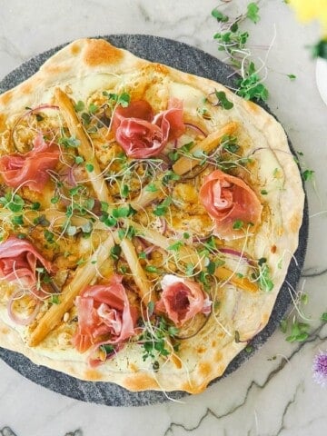 white asparagus flatbread on a stone platter with flowers on the side