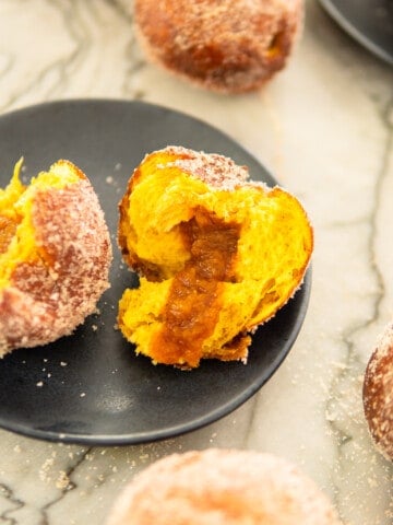 pumpkin donut torn in half sitting on a plate