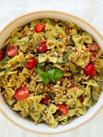 A bowl of pesto pasta salad with bright tomatoes poking through.