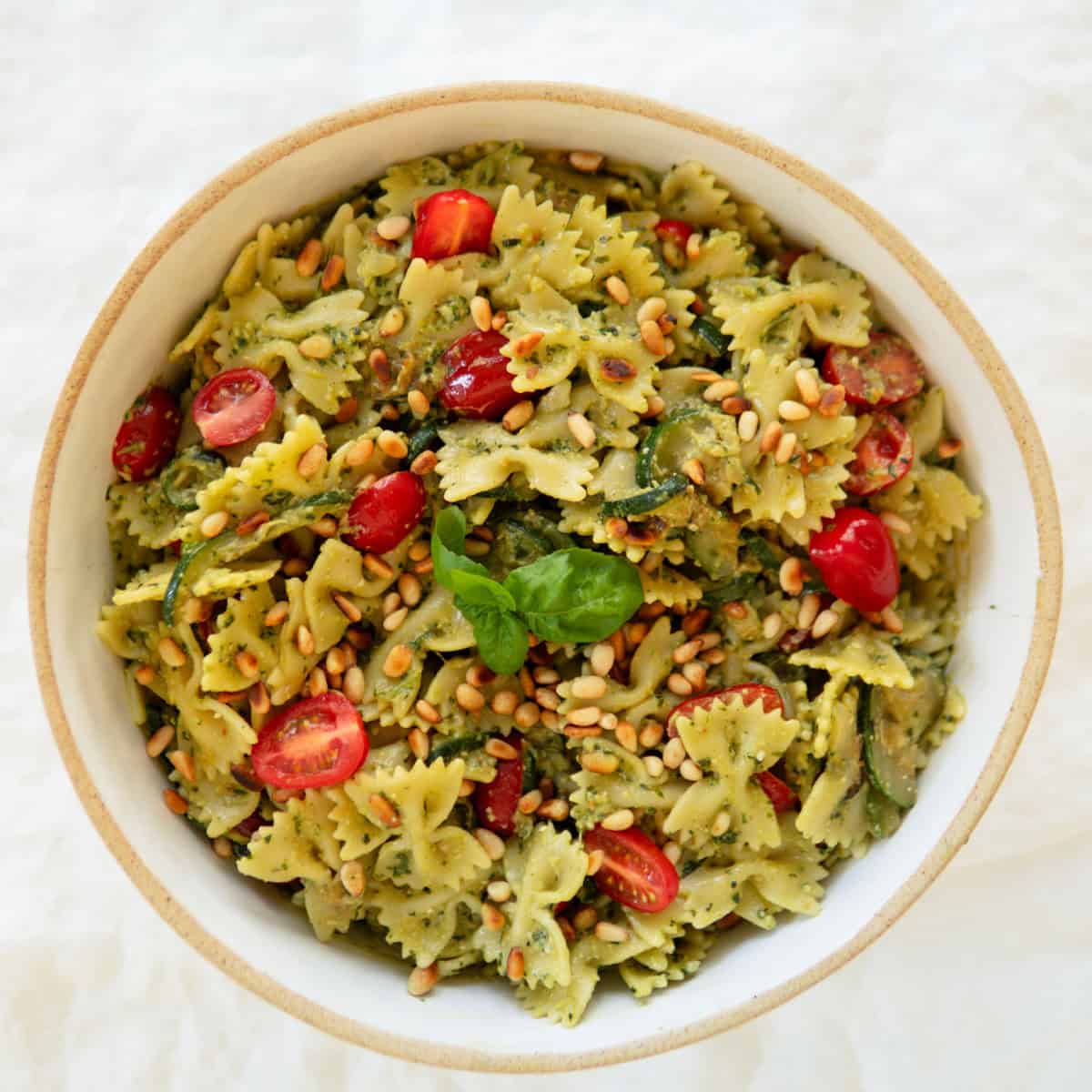 A bowl of pesto pasta salad with bright tomatoes poking through.