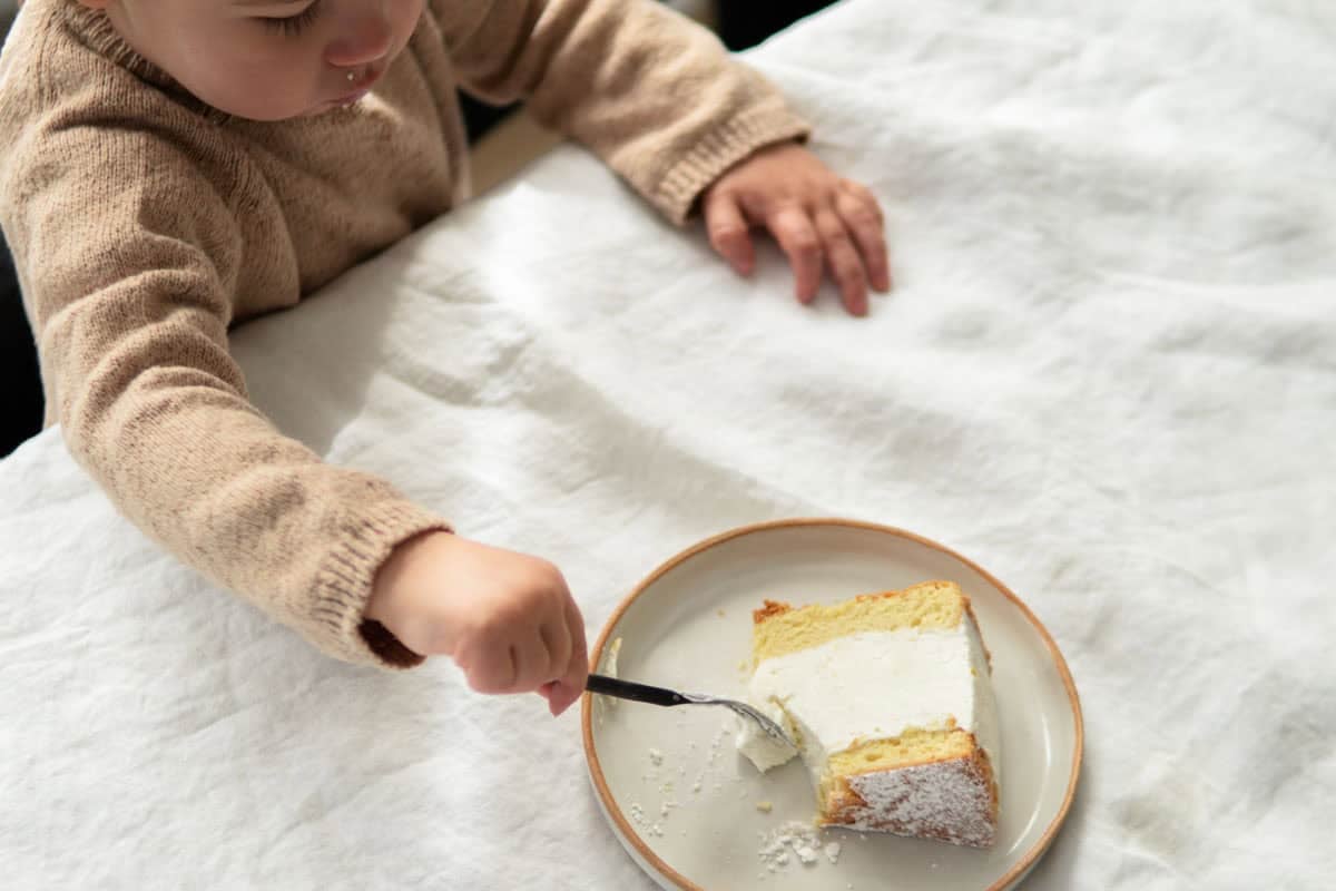 A small child eating a piece of German cheesecake with a fork.