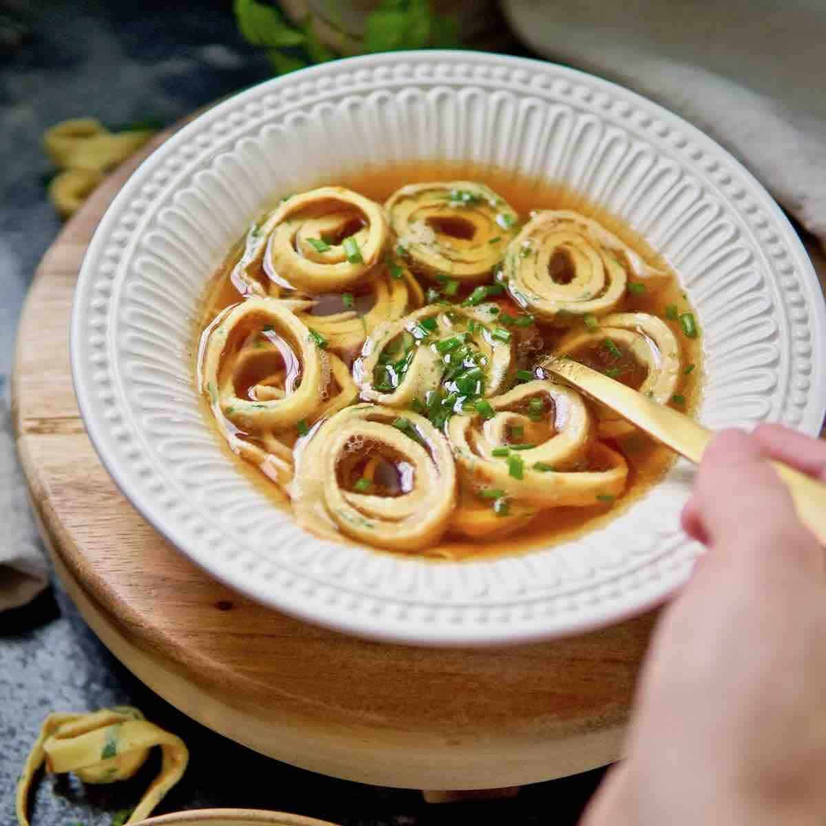 a bowl of German pancake soup and a hand reaching for a spoonful of soup