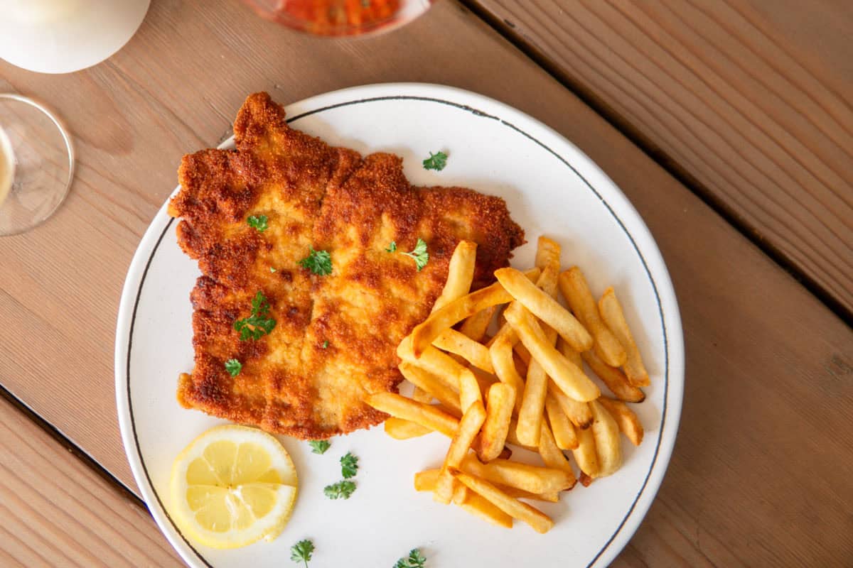 A golden schnitzel on a plate with fries.