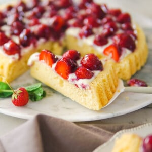 A whole German strawberry cake on a platter with a slice on a cake server in front.