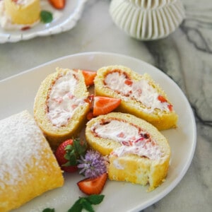 Strawberry cream cake roll on a white platter.