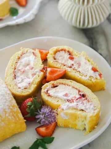 Strawberry cream cake roll on a white platter.
