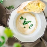 Creamy white asparagus soup in a bowl with a buttered slice of baguette.