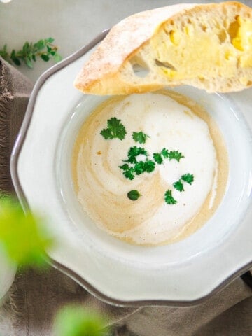 Creamy white asparagus soup in a bowl with a buttered slice of baguette.