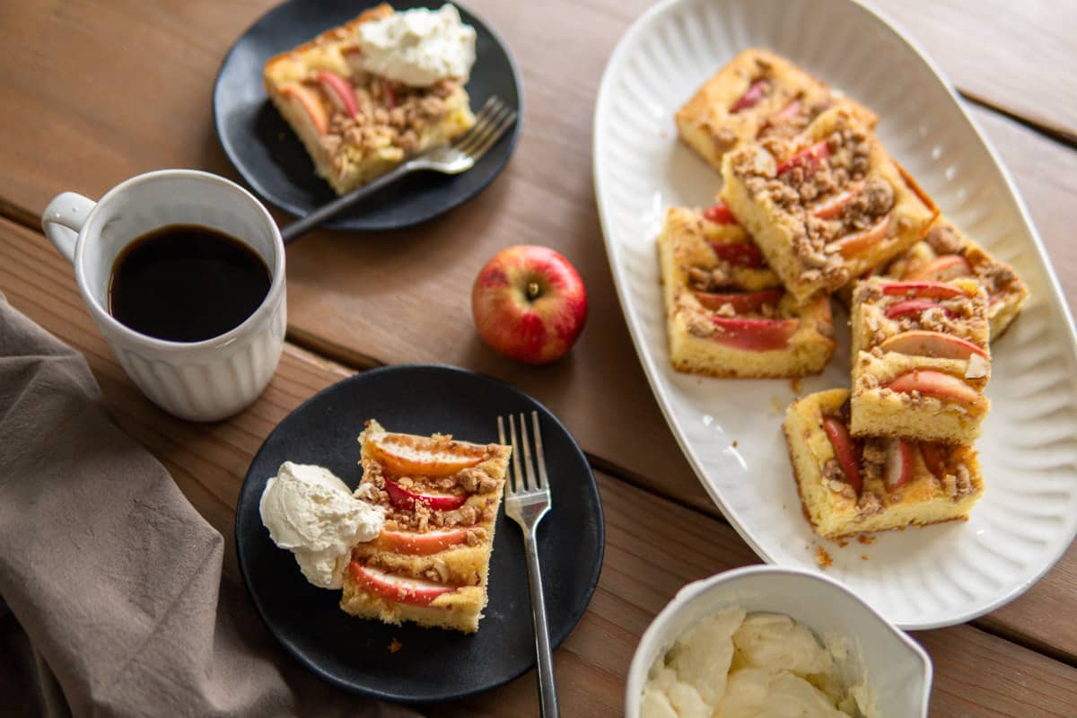 platter full of apple cake and slices of apples cake on plates with coffee mug