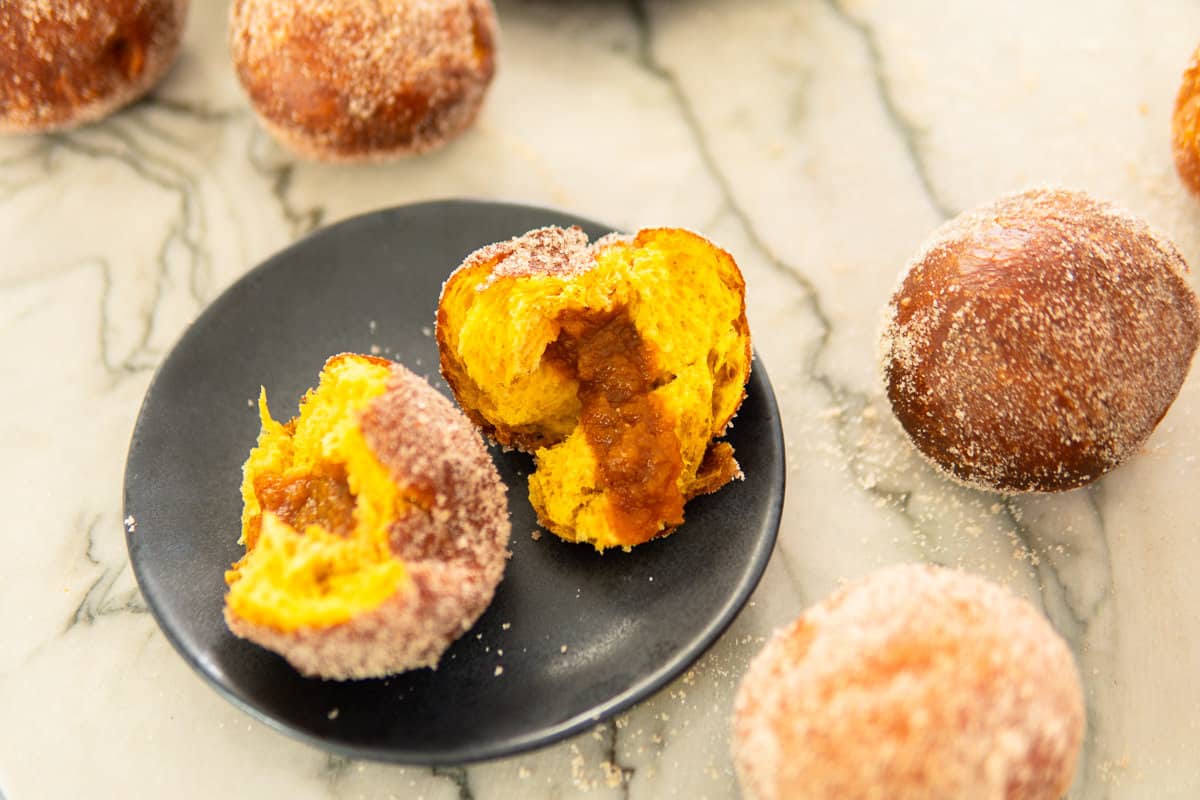 plate of a Pumpkin Berliner torn open on a plate surrounded by more German donuts