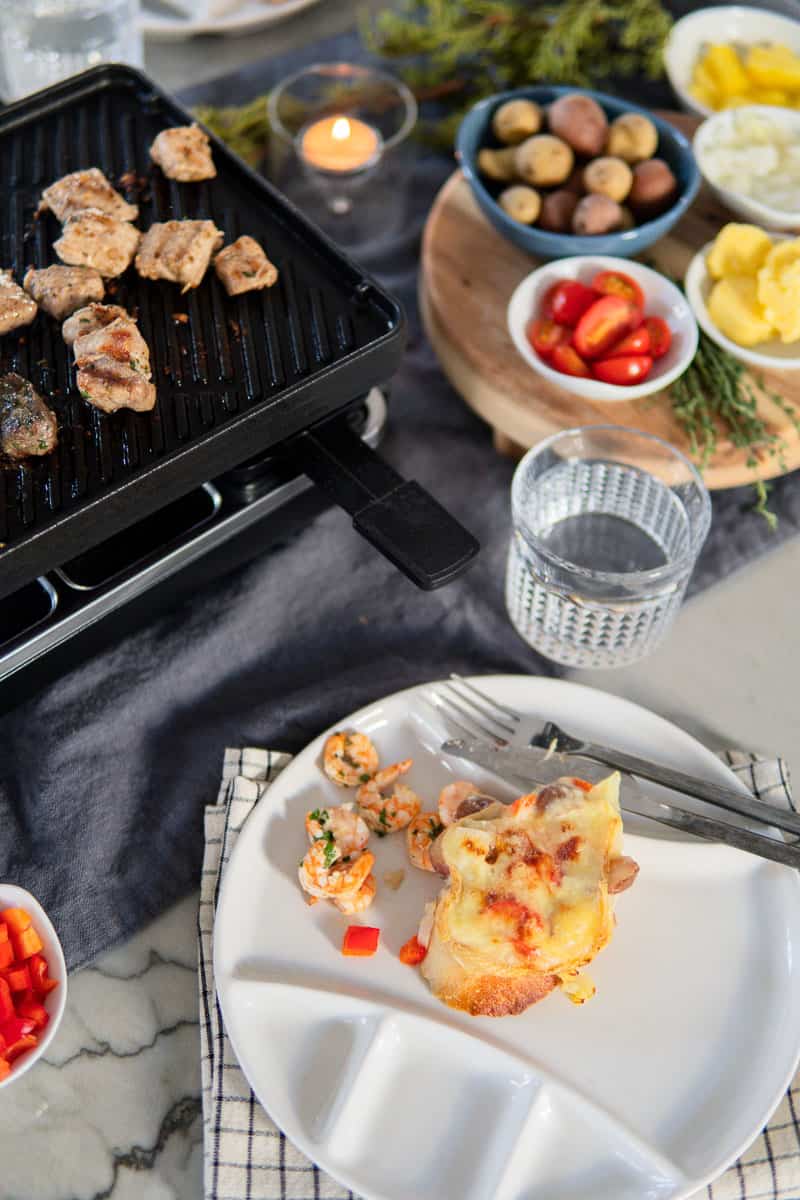 cheese and shrimp on plate and raclette grill behind it