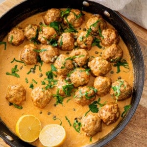 pan filled with German meatballs in sauce and garnished with parsley and lemon