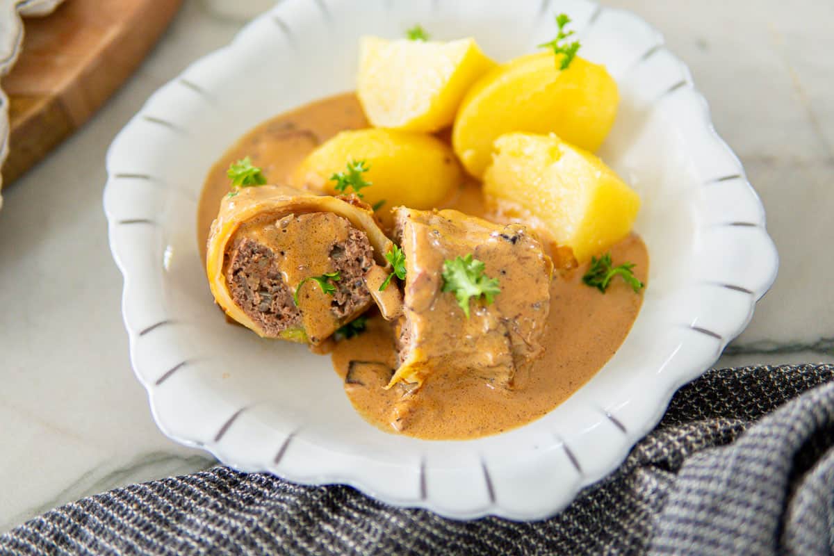 sauce-covered cabbage roll on a plate with boiled potatoes