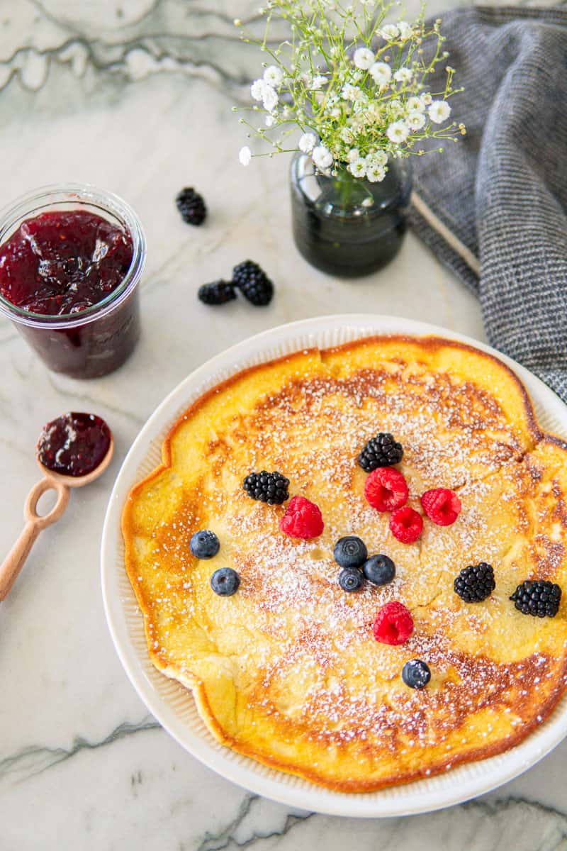 powdered sugar dusted German pancakes topped with fresh berries and with a side of strawberry jam