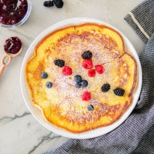 German pancake on a large plate topped with powdered sugar and berries