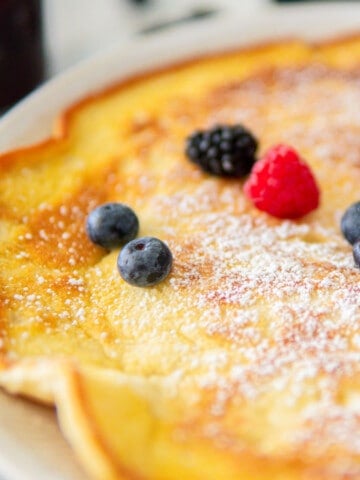 closeup of German pancakes dusted with powdered sugar and topped with fresh berries