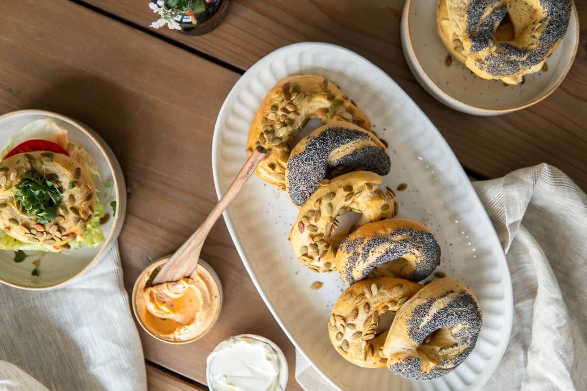 bagels on a platter with cream cheese next to s bagel sandwich on a plate