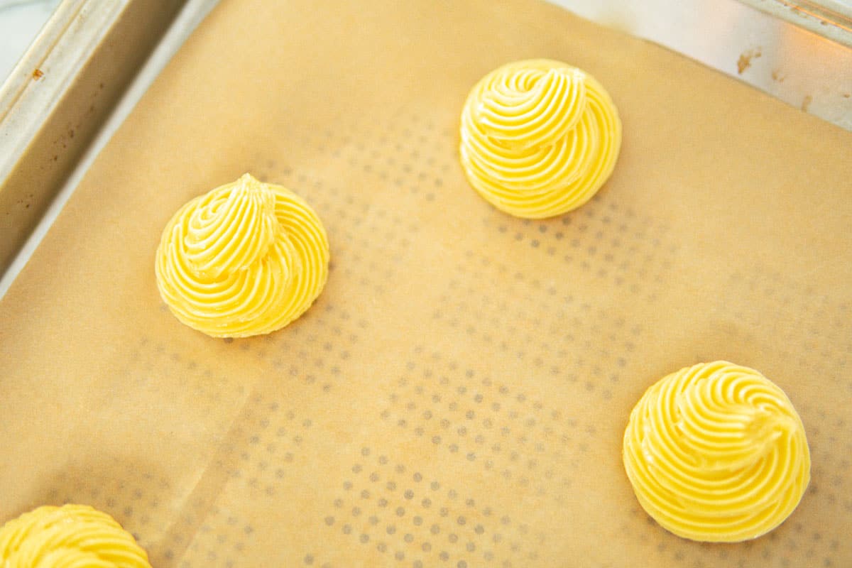 piping pate a choux on a baking sheet covered with parchment paper