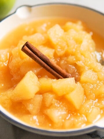 chunky apple sauce in a white dish with a cinnamon stick