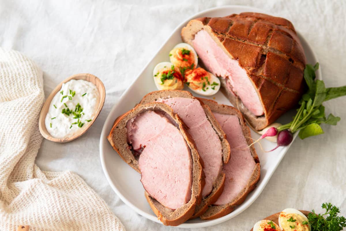 Baked ham in bread sliced open on a platter with some deviled eggs.