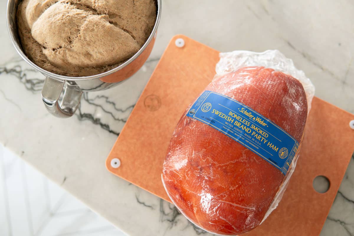 Schaller and Weber whole ham on a cutting board and some bread dough in a steel bowl next to it on the counter.