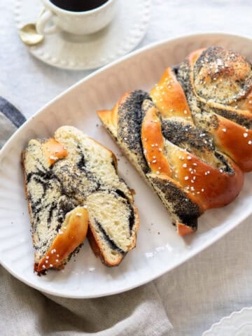 Braided bread with poppy seed filling cut into slices and a cup of coffee.