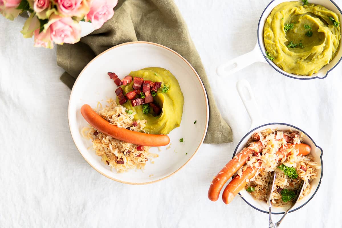 A plated dinner of mashed peas, sauerkraut and wiener sausages. Sides of sauerkraut and more pea puree.