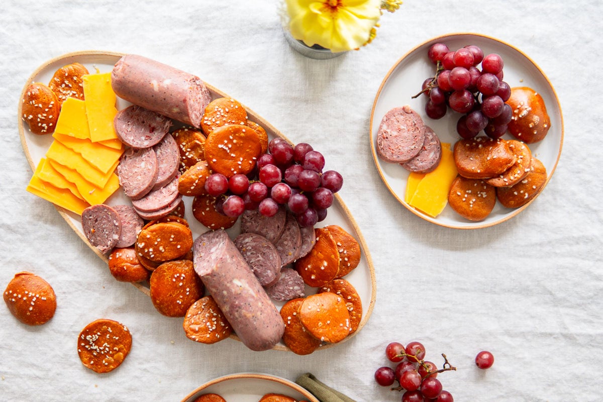 Pretzel crackers on a board with meats, cheeses and grapes.