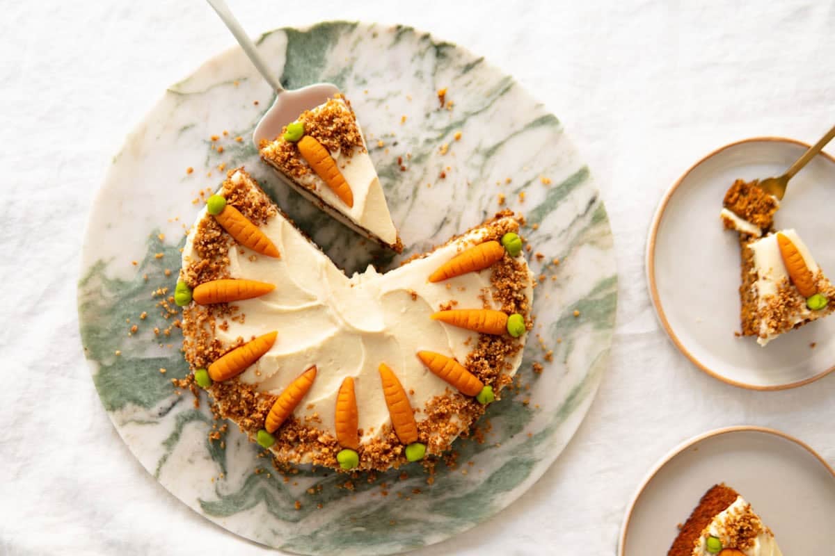 Gluten free carrot cake sitting on a cake platter with two plates of carrot cake next to it.