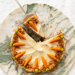 Swiss carrot cake decorated with marzipan carrots sitting on a marble cake platter.
