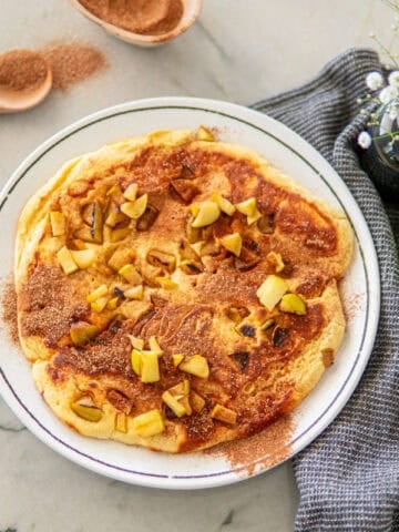 A large apple pancake sitting on a plate, topped with cinnamon sugar.