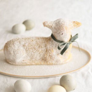 A lamb cake sitting on a cake platter surrounded by eggs for Easter.
