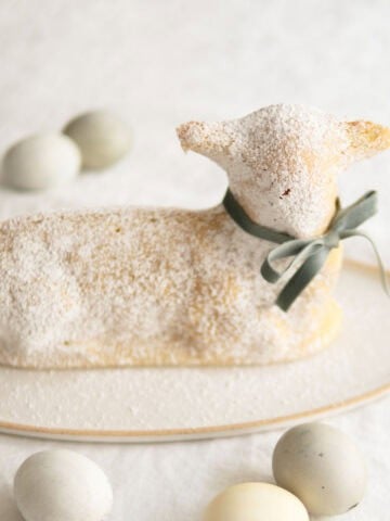 A lamb cake sitting on a cake platter surrounded by eggs for Easter.