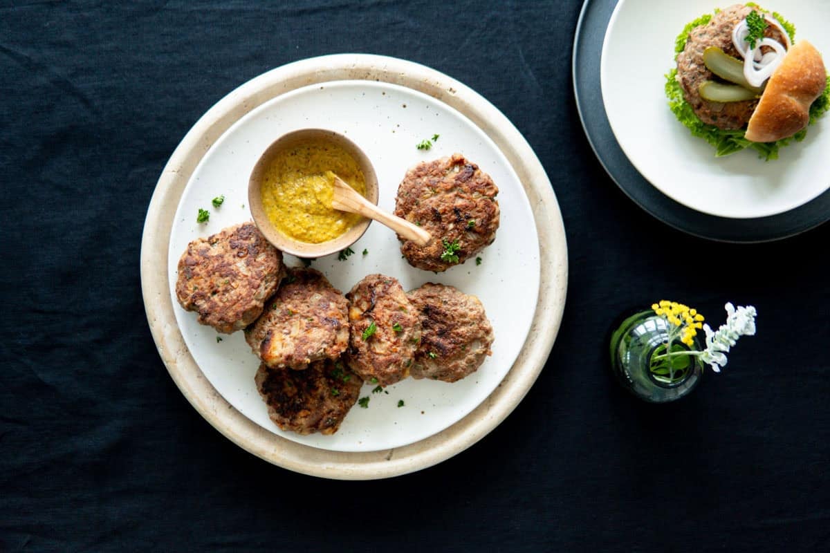 Frikadellen on a platter with a German hamburger on a bun on a plate next to it.