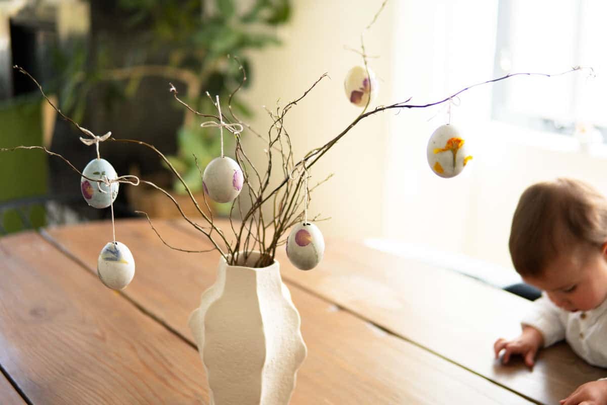 Decorated Easter eggs hanging from branches that are placed inside of a vase.