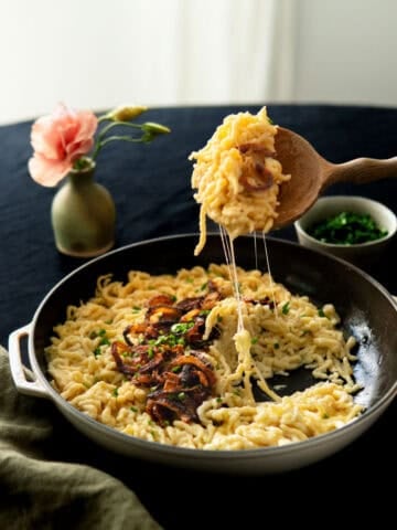 a cast iron dish filled with kaesespaetzle and topped with caramelized onion and chives