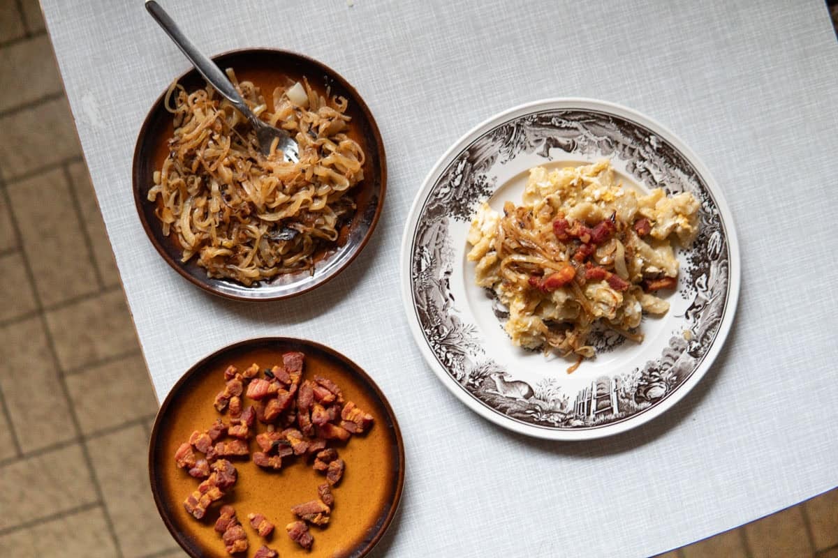 Omas Kloesschen on a plate next to a plate of caramelized onion and crisp bacon.