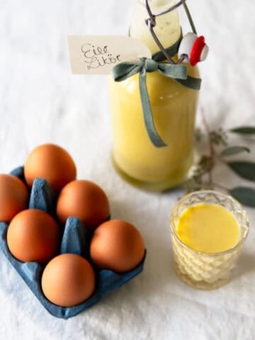 Homemade spiked egg nog in a glass bottle with some eggs on the side.