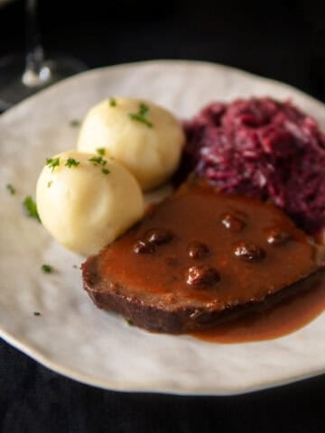 Sauerbraten slice on a plate with sauce, potato dumplings and red cabbage.