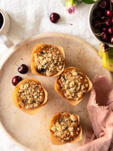 Banana muffins with cherries on a platter with a cup of coffee next to it.
