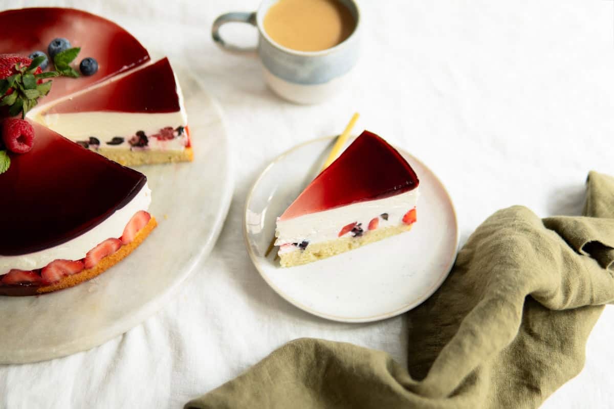 A slice of yogurt berry cake on a small plate with a cup of coffee.