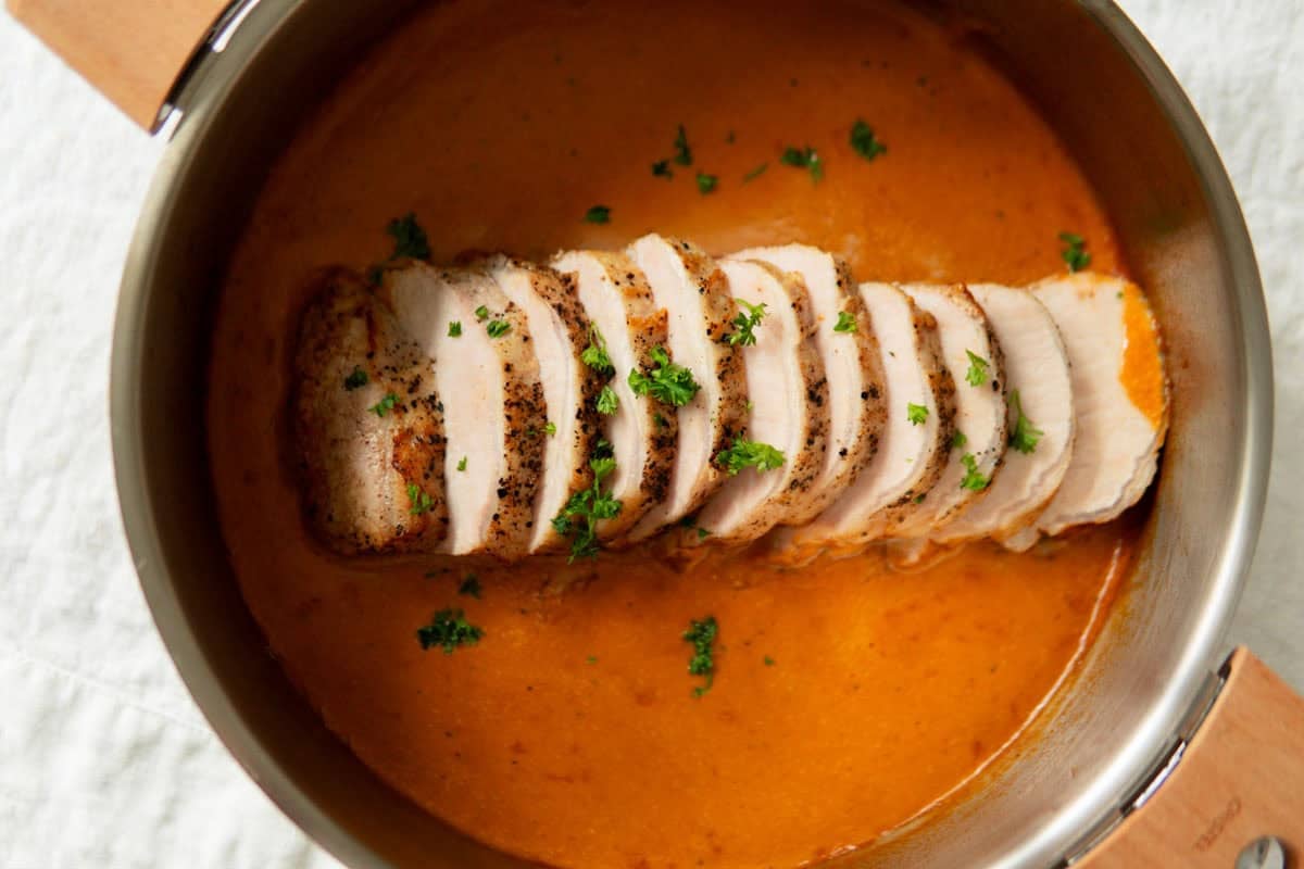 Closup of sliced German pork loin roast sitting in a pan with sauce.
