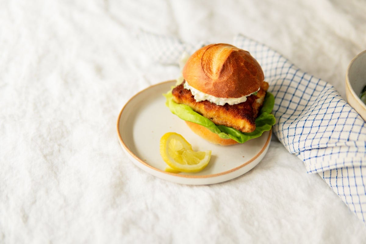 Assembled German fried fish sandwich with remoulade sauce and a slice of lemon on the plate.