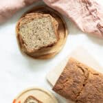 Top view of whole grain bread with seeds sitting on a cutting board and slices of bread stacked up next to it.