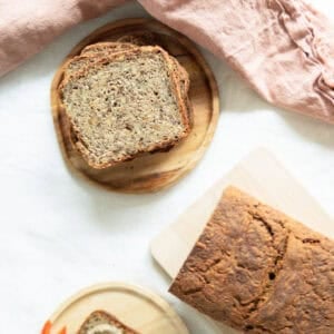 Top view of whole grain bread with seeds sitting on a cutting board and slices of bread stacked up next to it.